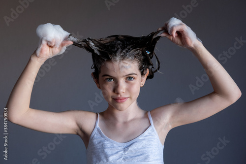 Obraz na płótnie little / young girl washes her hair, soap suds from shampoo on her head, portrait. Child makes horns from hair w salonie