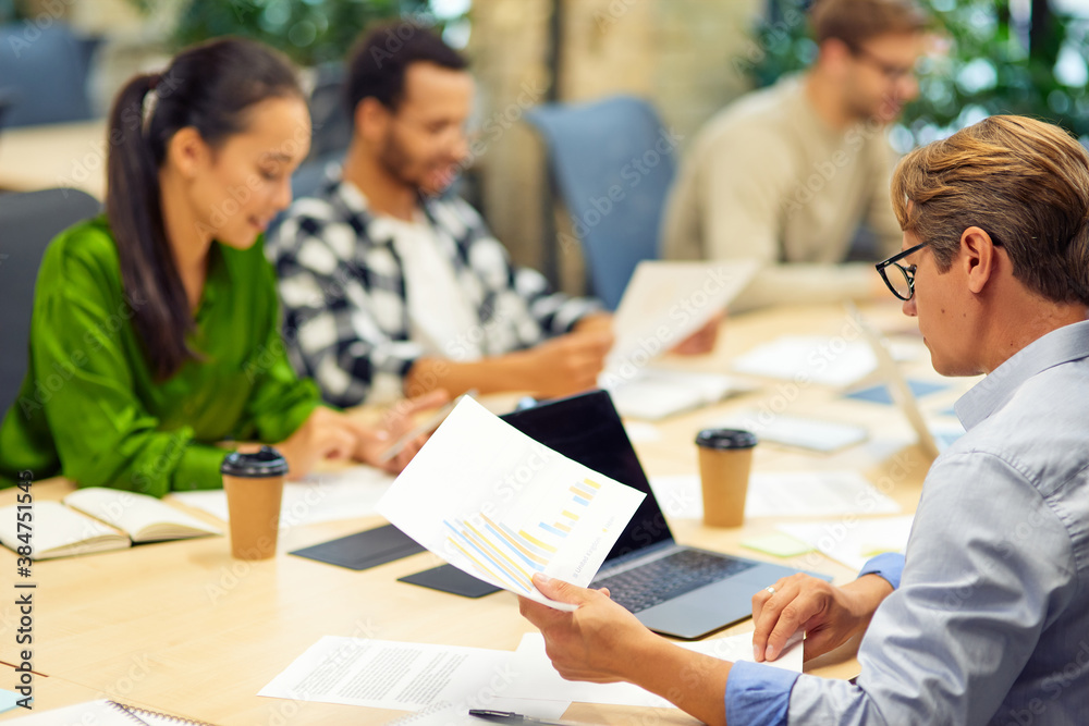 Brainstorming meeting. Group of multiracial people sitting at the desk in the modern coworking space or office and working on project together Brainstorming meeting. Group of multiracial people sitting at the desk in the modern coworking space or office and working on project together