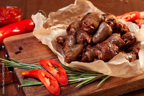Fried chicken hearts with vegetables and spices on a wooden board.