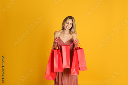 Happy young woman with shopping bags on yellow background. Black Friday Sale