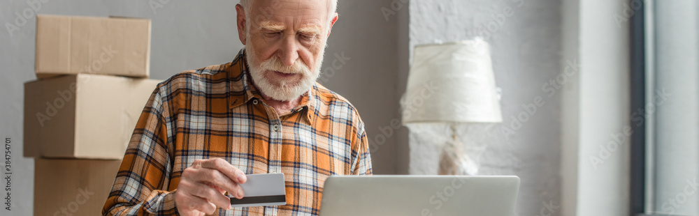 panoramic shot of senior man making online purchase with credit card and laptop panoramic shot of senior man making online purchase with credit card and laptop