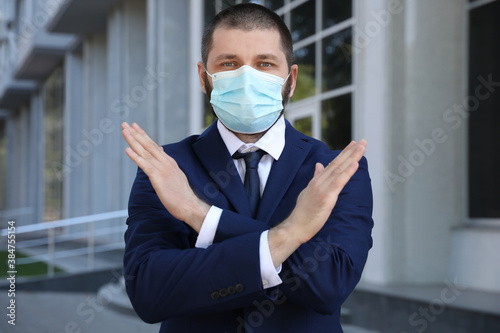 Man in protective face mask showing stop gesture outdoors. Prevent spreading of coronavirus