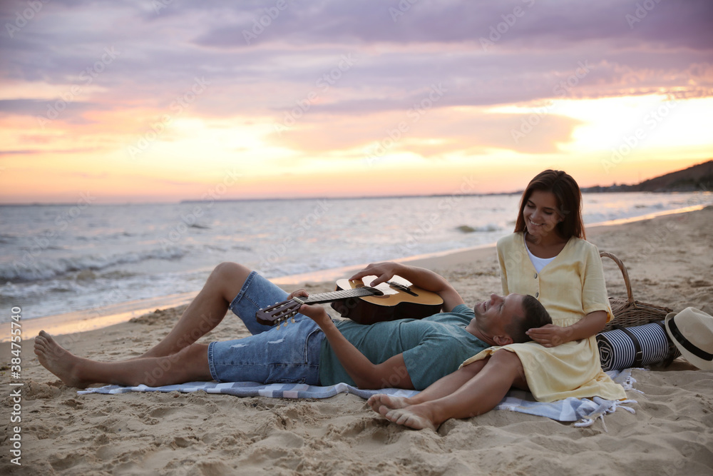 Lovely couple with guitar and picnic basket on beach at sunset