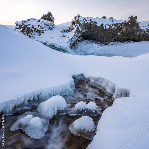 A small stream by Geitafoss waterfall in winter. Fresh snow cover on ground with blue light of winter dawn. North Iceland. photo