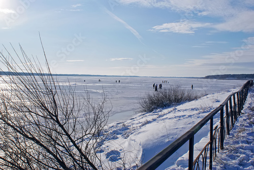 People of all ages walk on the ice and fish in winter  on a Sunny day off  on a frozen lake. Winter holidays  winter landscape