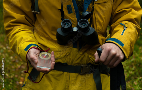 the man went hiking in the forest. In his hands he holds a compass, binoculars and a trekking stick close-up