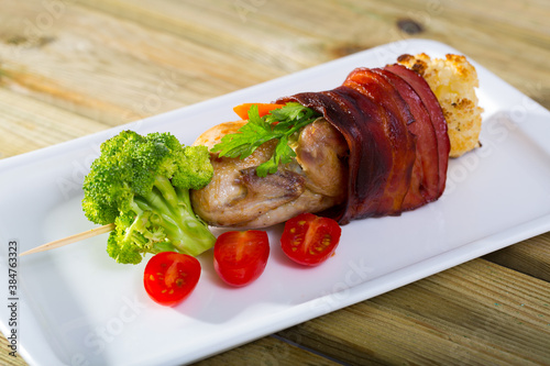 Grilled quail with Iberian ham fried on skewers with vegetables, served on plate