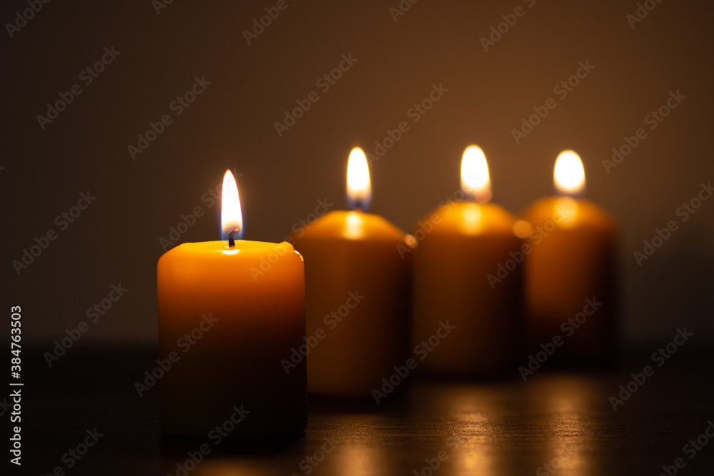 Row of lit candles burning in the darkness. Golden tones with selective focus on candle and background blur Row of lit candles burning in the darkness. Golden tones with selective focus on candle and background blur