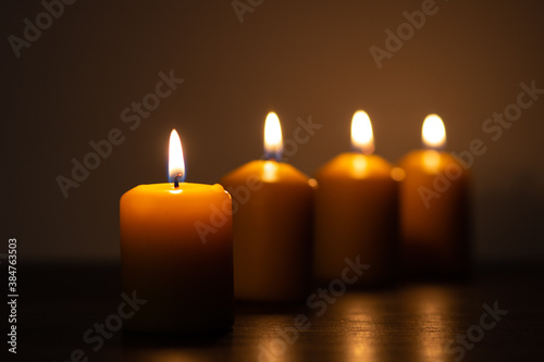 Row of lit candles burning in the darkness. Golden tones with selective focus on candle and background blur