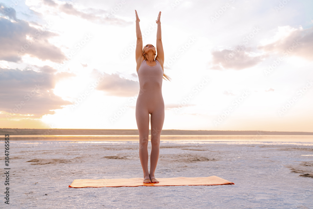 Young woman practicing yoga while doing workout on fitness mat outdoors