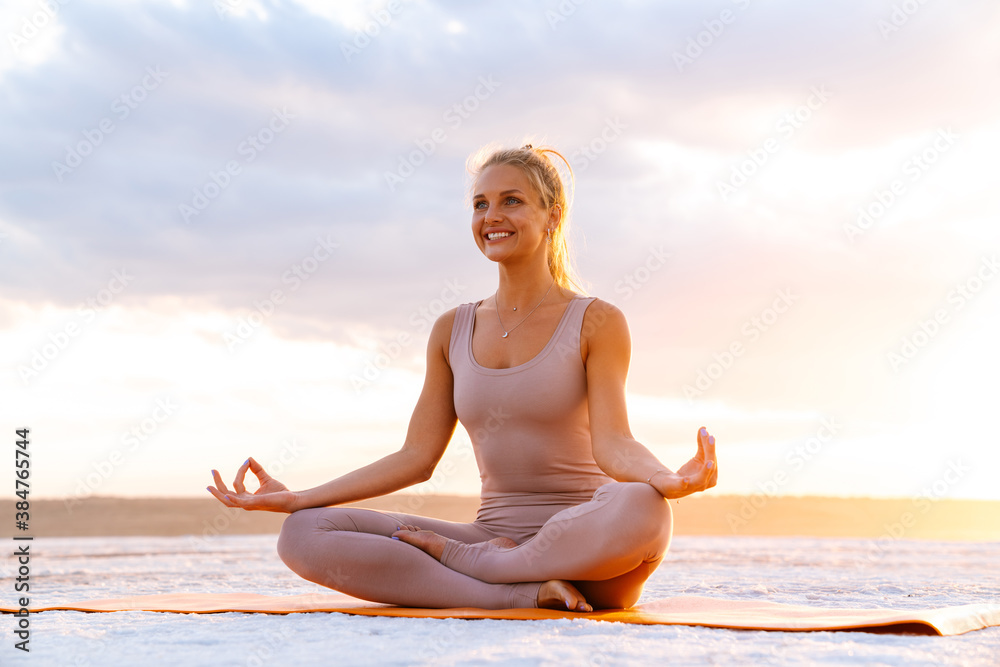 Young woman practicing yoga while doing workout on fitness mat outdoors
