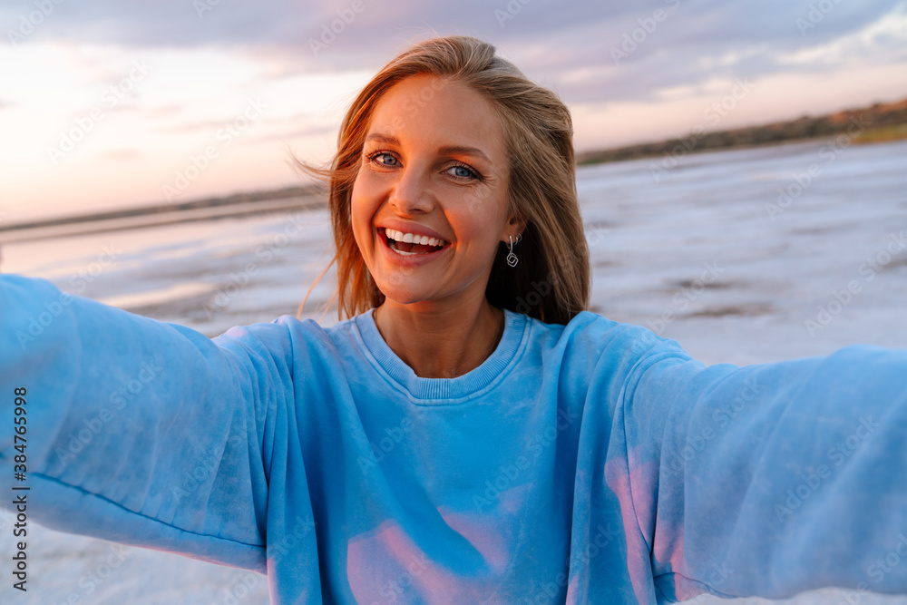 Young happy woman smiling at camera while taking selfie outdoors