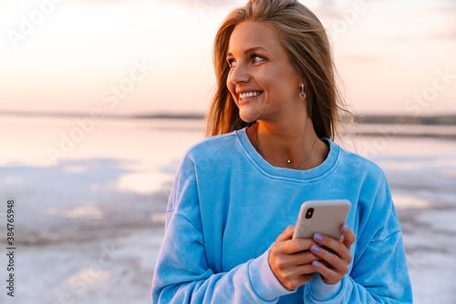 Young caucasian happy woman smiling and holding cellphone outdoors