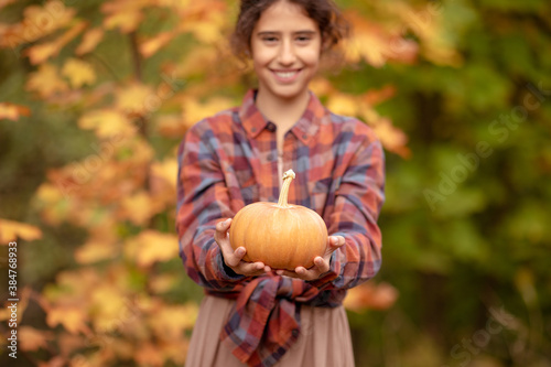 A girl holds a small pumpkin in her hands. Shallow depth of field.