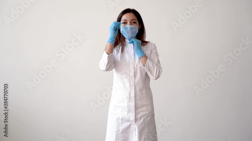 Female doctor putting on medical mask and making the OK gesture. Copy space. Front view and white background.