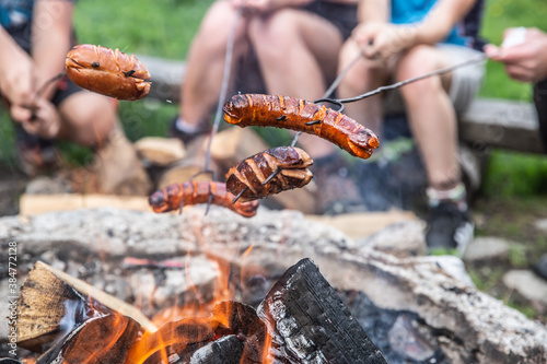 Friends roast sausages over an open fire outdoors