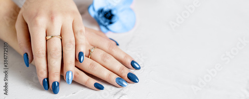 Beautiful hands with trendy classic blue manicure lying on a white stone