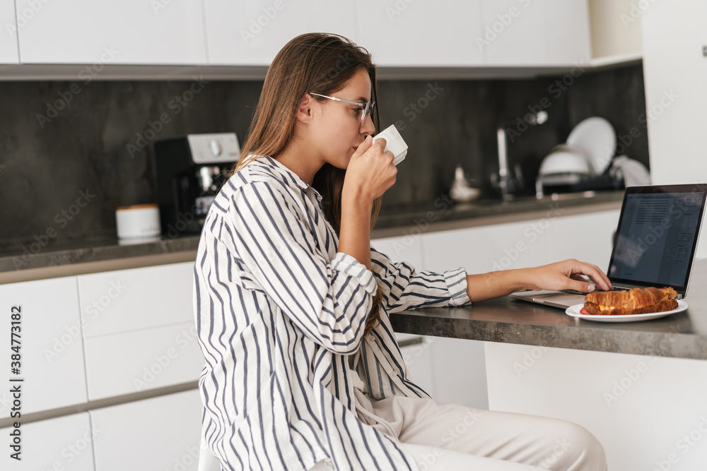 Young caucasian woman drinking coffee while working on laptop at home Young caucasian woman drinking coffee while working on laptop at home