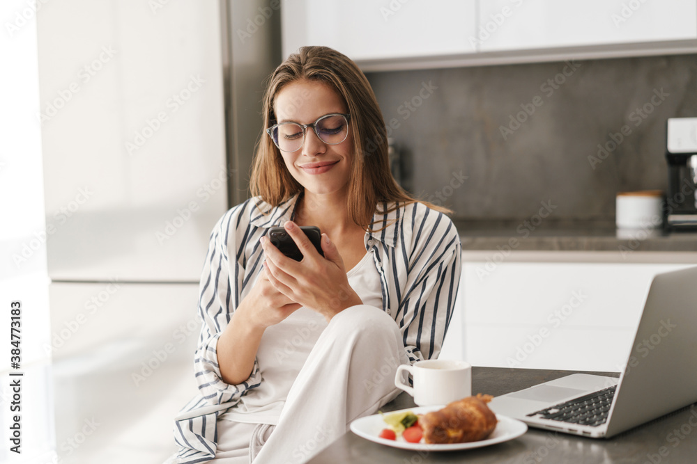 Young caucasian woman holding cellphone while having breakfast at home Young caucasian woman holding cellphone while having breakfast at home