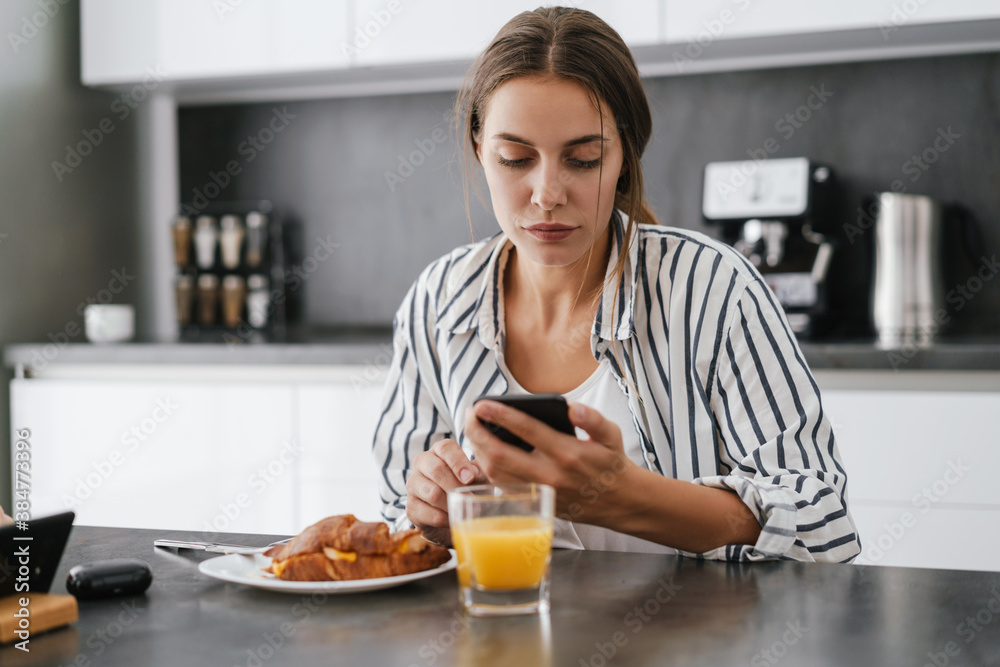 Young caucasian woman holding cellphone while having breakfast at home