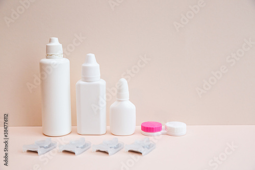 Contact lenses, lens solution and lens containers on a light pink background. Health care concept