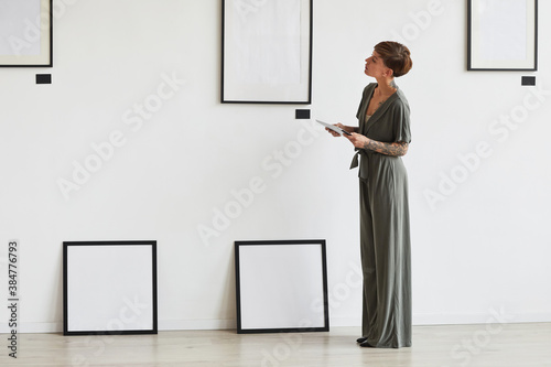 Graphic full length portrait of elegant female art gallery manager looking at frame setting while planning exhibition or event, copy space