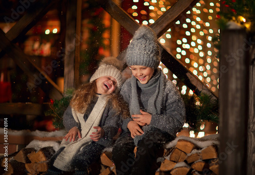 Young boy and girl sitting on logs before home terrace with Christmas background