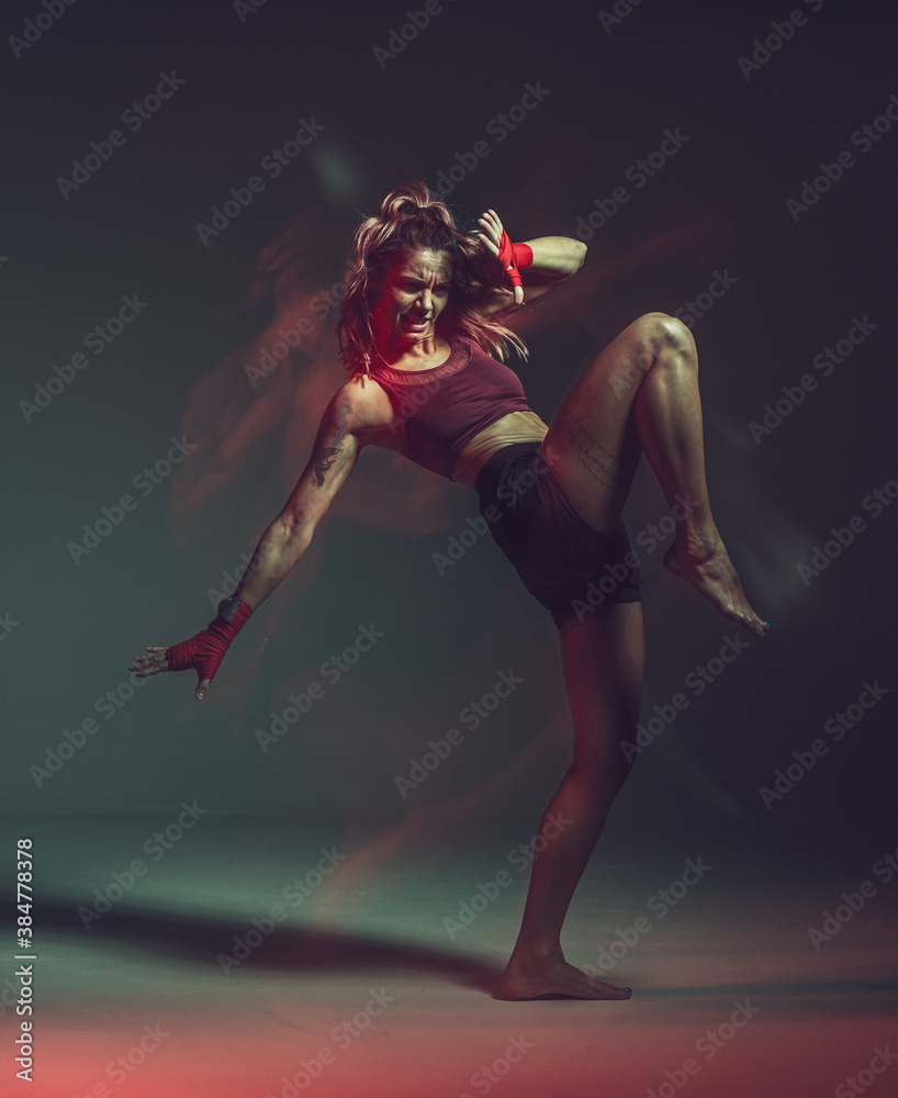 Cool female fighter in boxing bandages trains knee kick. Mixed martial arts poster. Long exposure shot