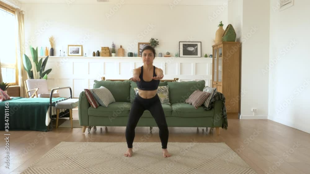 Strong girl student is squatting at home standing on floor of beautiful light flat focused on exercise. Woman is wearing trendy leggings, short top Strong girl student is squatting at home standing on floor of beautiful light flat focused on exercise. Woman is wearing trendy leggings, short top