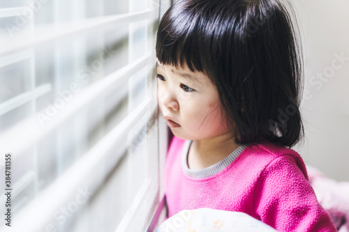 Картината върху платно Cute Asian little kid girl toddler sad unhappy crying against window looking out
