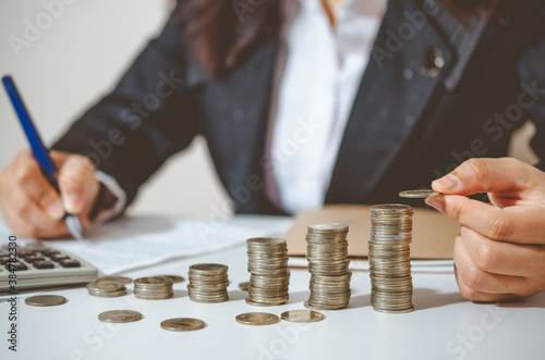 Closeup image businesswoman holding coins putting to stacking coins bank and calculating. concept saving money wealth for finance accounting.
