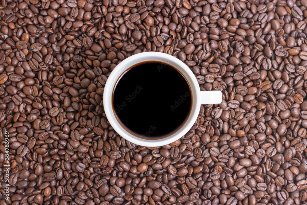 TOP VIEW OF A COFFEE BEANS BACKGROUND AND A FULL CUP OF COFFEE IN THE MIDDLE TOP VIEW OF A COFFEE BEANS BACKGROUND AND A FULL CUP OF COFFEE IN THE MIDDLE