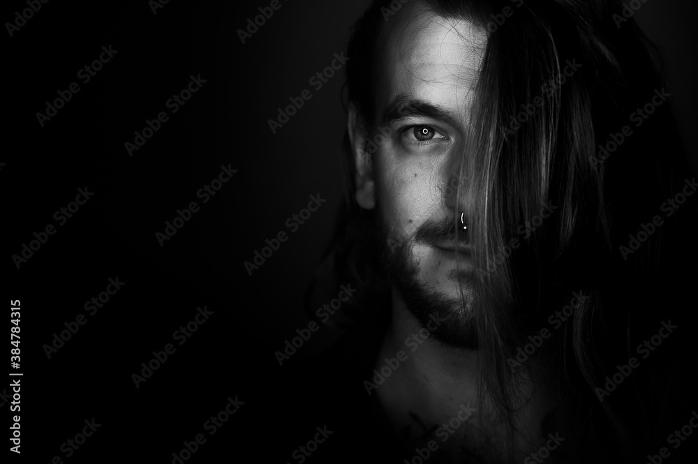 A young man looks at the camera. Half of his face is covered by his long hair. A young man looks at the camera. Half of his face is covered by his long hair.