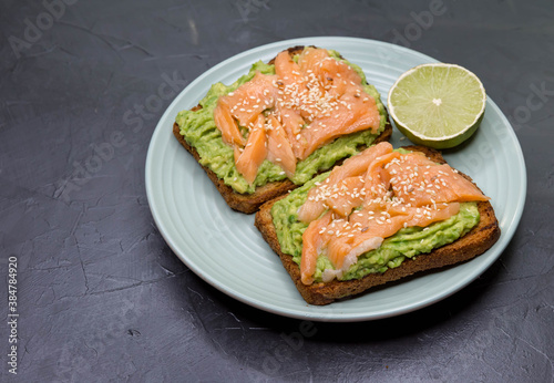Toasted bread with avocado, red fish on dark background. Breakfast