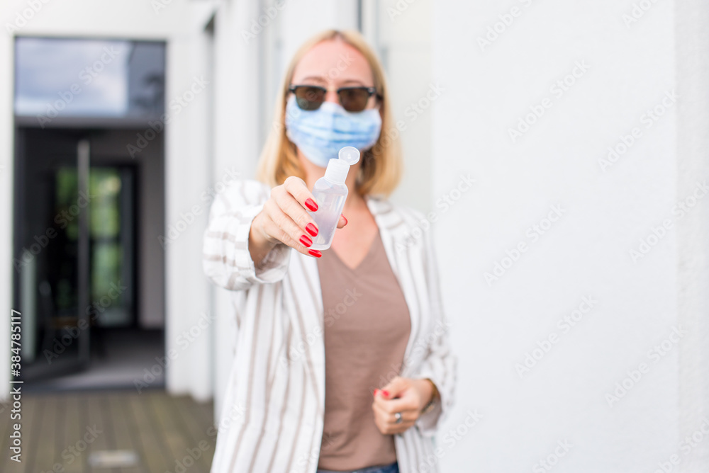 A young woman in an anti-covid mask stands on a terrace of her house, holding a disinfectant gel in her hands. Woman in terrace with sanitizer gel. Woman in quarantine on terrace. Pandemic theme