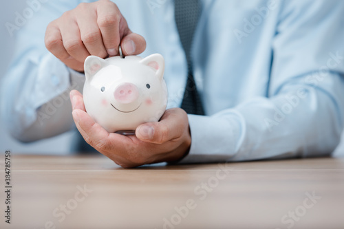 business finance saving and investment concept. male hand put money coin into piggy bank for saving money wealth.