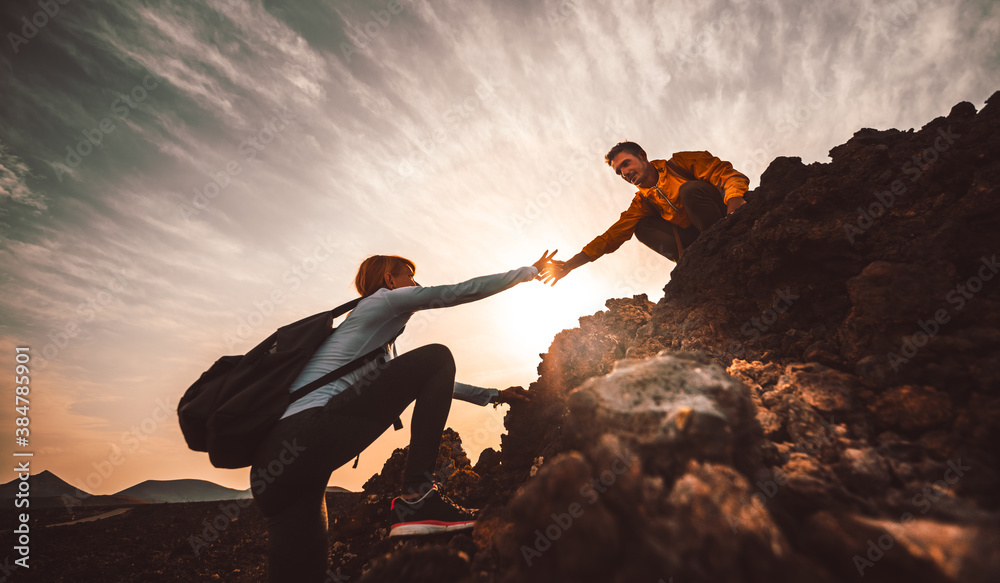 Couple of hikers helping each other climbing a mountain at sunset