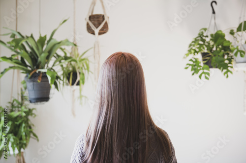 観葉植物に囲まれた、秋冬ニット服を来た綺麗な髪の女性の後ろ姿