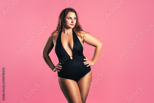 Sexy plus size fashion model in black one-piece swimsuit, fat woman in lingerie on pink background © staras