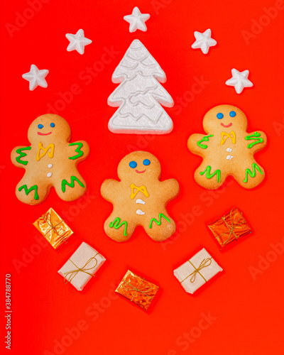 Three gingerbread men are arranged on a red background along with gifts and a Christmas tree. Christmas New Year concept. There is a place for the text