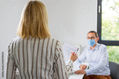 The woman is giving a presentation and the man wearing the face mask. Two business colleagues wearing protective face mask on a meeting during coronavirus. Work in a corporation during a pandemic. 