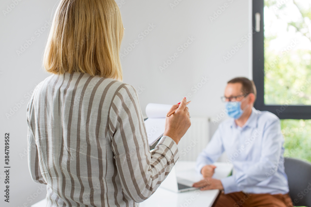 Fototapeta premium The woman is giving a presentation and the man wearing the face mask. Two business colleagues wearing protective face mask on a meeting during coronavirus. Work in a corporation during a pandemic. 