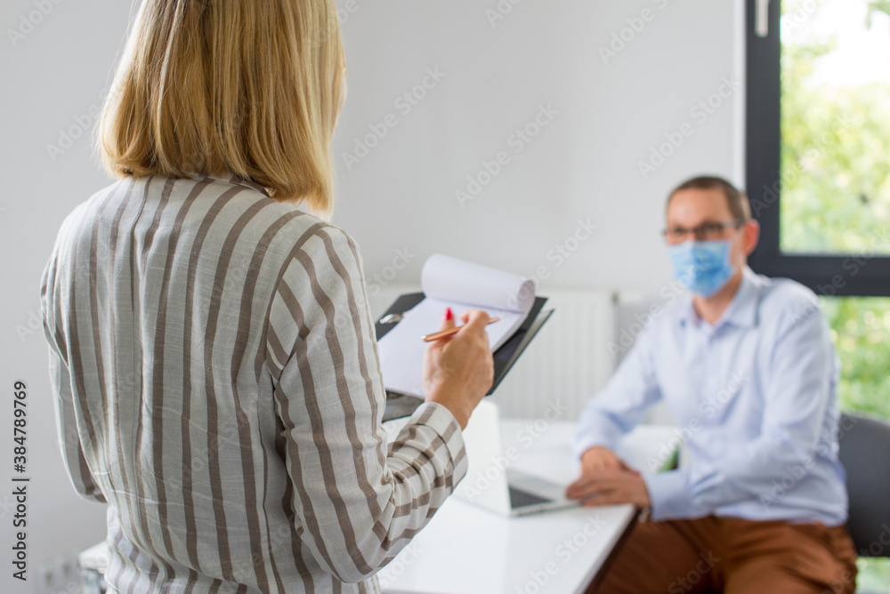Obraz premium The woman is giving a presentation and the man wearing the face mask. Two business colleagues wearing protective face mask on a meeting during coronavirus. Work in a corporation during a pandemic. 