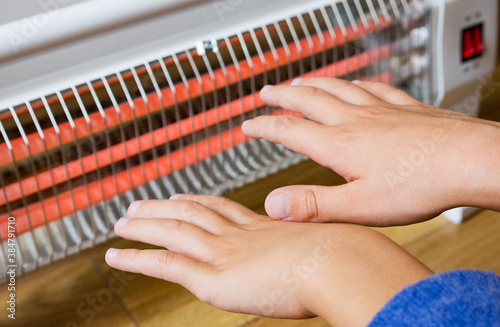 Hands warming up near home heater at winter cold time. The symbolic image of the heating season at home. 