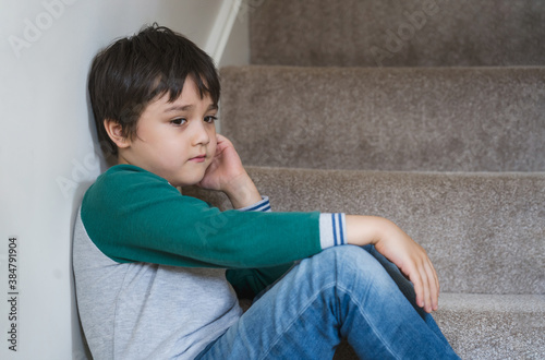 Sad asian boy sitting alone on staircase in the morning, Lonely kid looking dow with sad face not happy to go back to school, Depressed child boy sitting in the corner of a stair,Mental health
