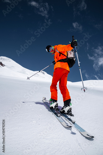 Ascent of a skier with a backpack in a mask and sunglasses on skis with poles to go uphill for freeride and backcountry. North Caucasus. Climbing Volcano Elbrus
