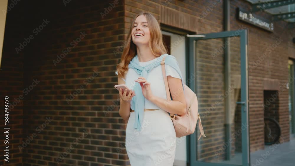 Stylish young attractive woman walking look around smiling use phone in city center outdoors. Happy girl with cellphone message communication portrait. Close up. Slow motion
