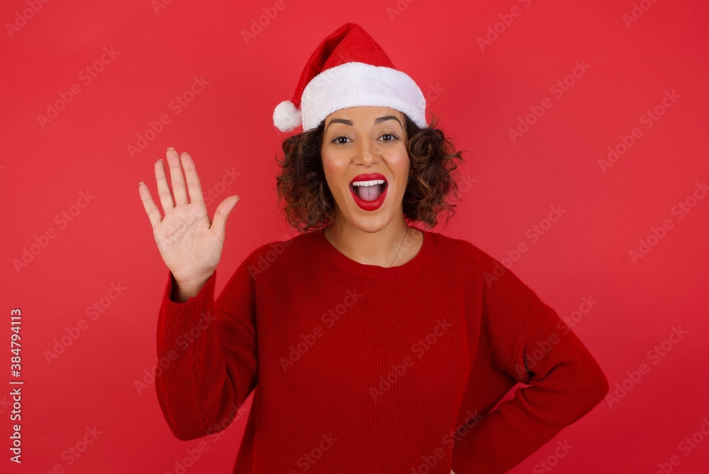 Young beautiful woman wearing Christmas hat standing over red isolated background Waiving saying hello or goodbye happy and smiling, friendly welcome gesture Young beautiful woman wearing Christmas hat standing over red isolated background Waiving saying hello or goodbye happy and smiling, friendly welcome gesture