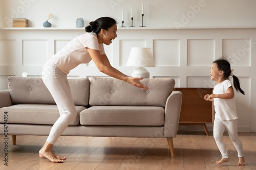 Overjoyed Asian mother and little girl enjoying funny activity together, dancing, running in living room, happy young mum and adorable toddler daughter enjoying leisure time at home, playing game photo