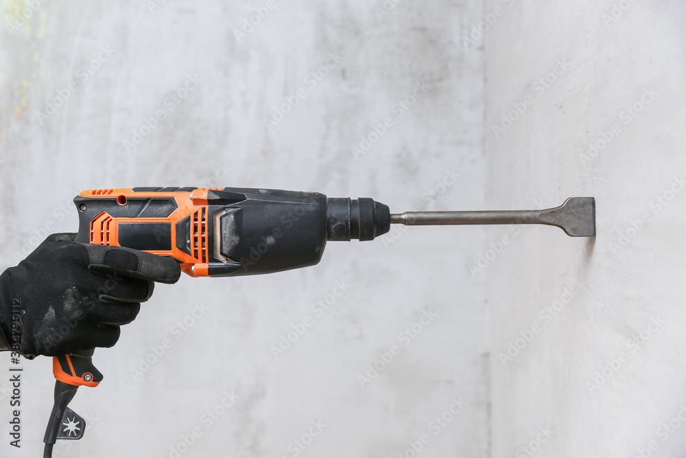 hands of a worker hold a hammer drill close-up on a gray wall background